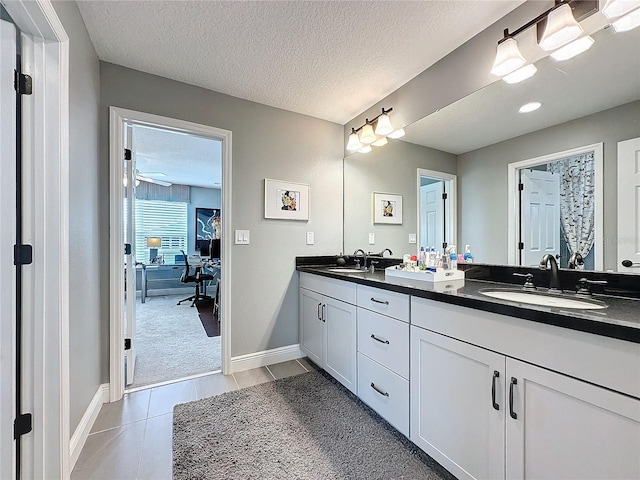 ensuite bathroom with double vanity, a textured ceiling, a sink, and tile patterned floors