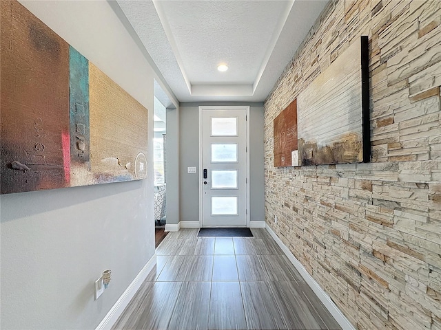 entryway with a textured ceiling, a raised ceiling, tile patterned floors, and baseboards