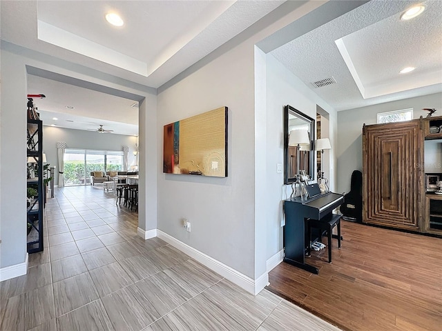 hallway featuring visible vents, baseboards, a tray ceiling, a textured ceiling, and recessed lighting