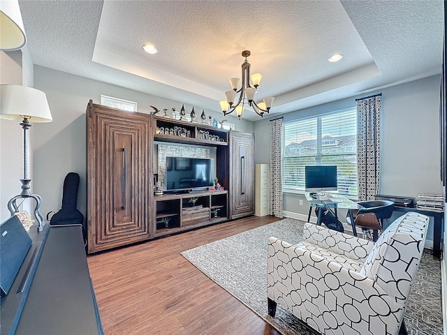 living room featuring a textured ceiling, a notable chandelier, wood finished floors, baseboards, and a raised ceiling