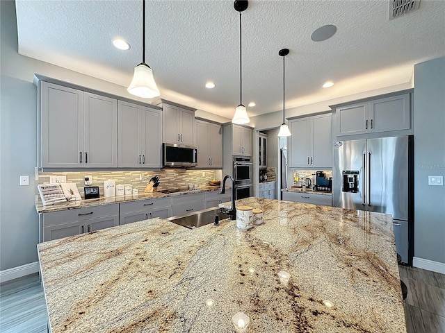 kitchen featuring a sink, visible vents, hanging light fixtures, appliances with stainless steel finishes, and light stone countertops