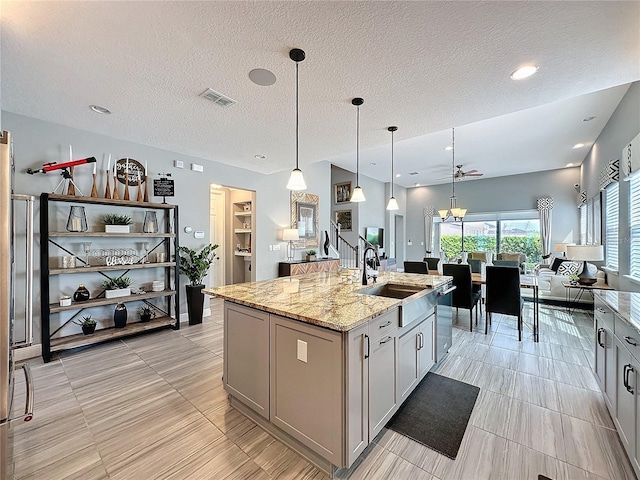 kitchen with decorative light fixtures, a sink, a center island with sink, and light stone countertops