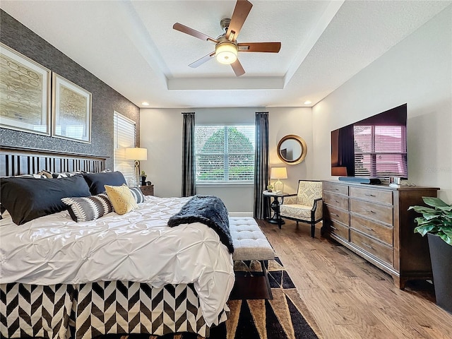 bedroom featuring ceiling fan, a tray ceiling, and light wood-style flooring