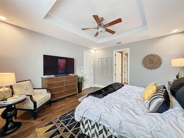 bedroom featuring visible vents, dark wood finished floors, a ceiling fan, baseboards, and a tray ceiling