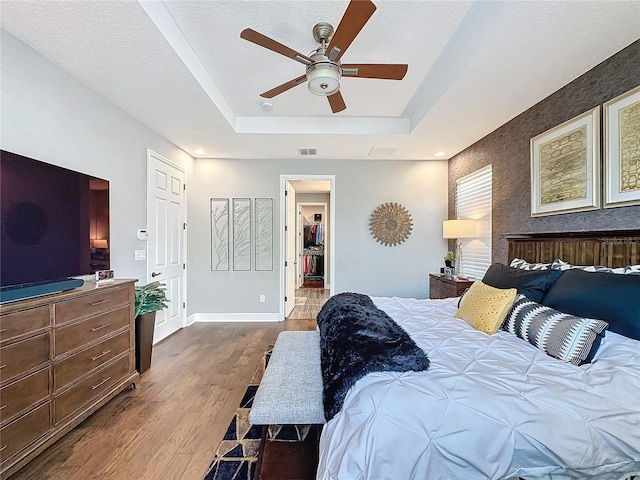 bedroom featuring a tray ceiling, visible vents, a textured ceiling, wood finished floors, and baseboards