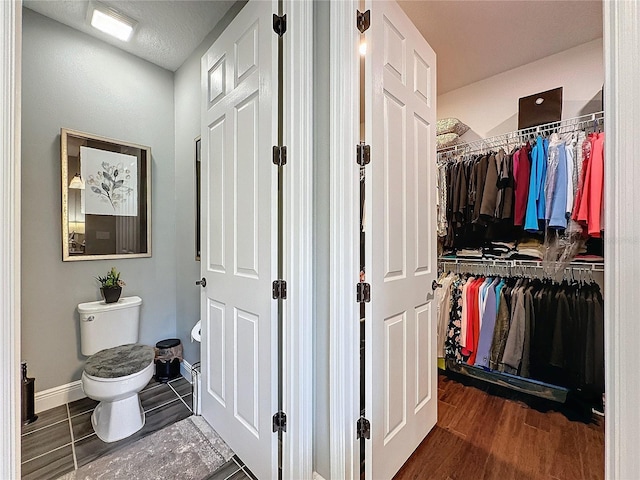 bathroom with a walk in closet, baseboards, toilet, and wood finished floors