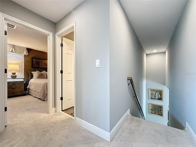 hall with light carpet, visible vents, an upstairs landing, and baseboards