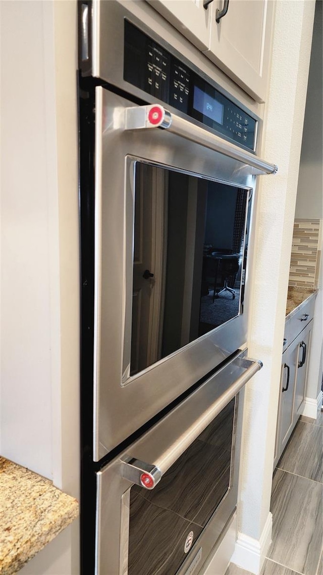 interior details featuring light stone counters, decorative backsplash, white cabinets, and stainless steel double oven