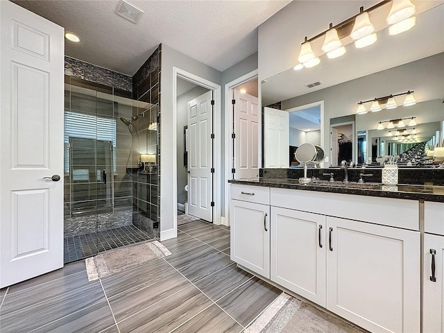 bathroom with a shower stall, visible vents, a textured ceiling, and vanity