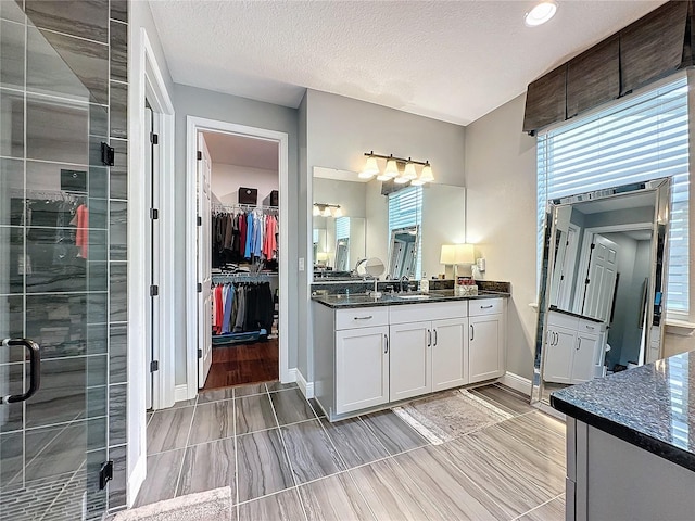 bathroom with baseboards, a shower stall, vanity, and a textured ceiling