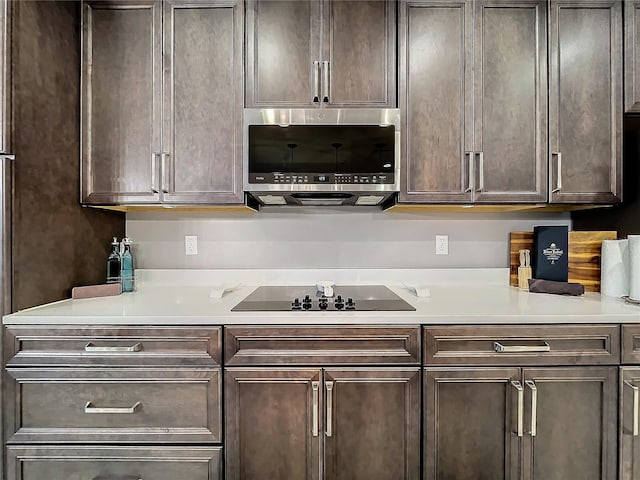 kitchen with black electric stovetop, stainless steel microwave, light countertops, and dark brown cabinets