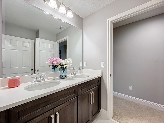 full bath featuring double vanity, a textured ceiling, visible vents, and a sink