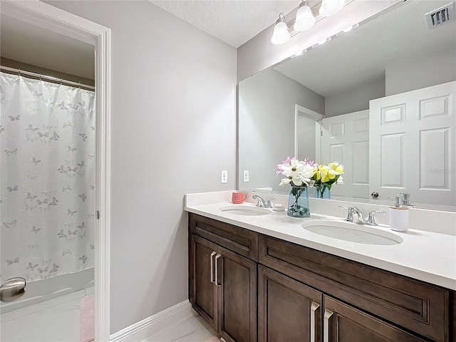 bathroom featuring visible vents, a sink, a textured ceiling, and double vanity