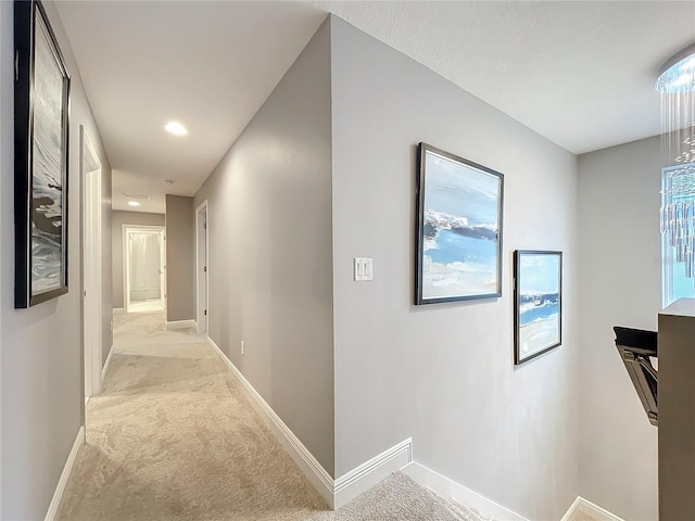 hall featuring light colored carpet and baseboards