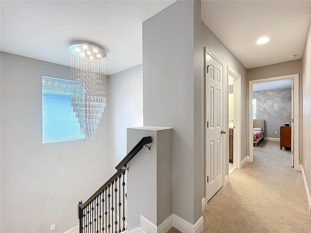 corridor featuring light carpet, an inviting chandelier, baseboards, and an upstairs landing