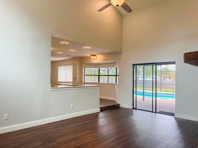 spare room with ceiling fan, dark wood-type flooring, a high ceiling, a sink, and baseboards