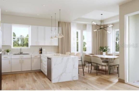 kitchen featuring light wood-style flooring, a peninsula, hanging light fixtures, white cabinetry, and a sink