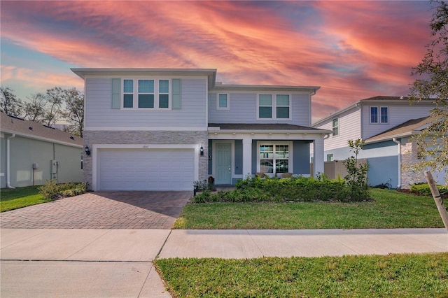 traditional home with a garage, stone siding, decorative driveway, and a front yard