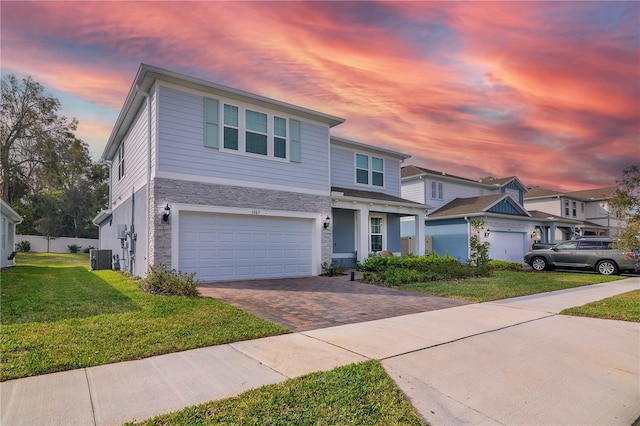 traditional home with decorative driveway, stone siding, a yard, and a garage