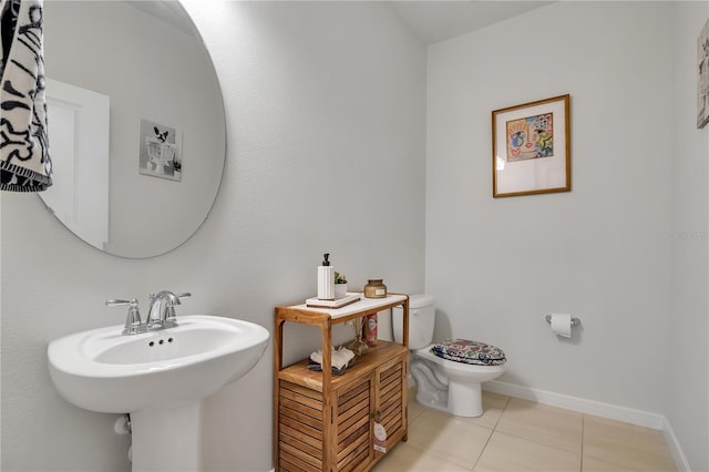 half bath featuring baseboards, a sink, toilet, and tile patterned floors