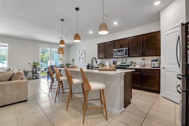 kitchen featuring a center island with sink, appliances with stainless steel finishes, open floor plan, decorative light fixtures, and light countertops