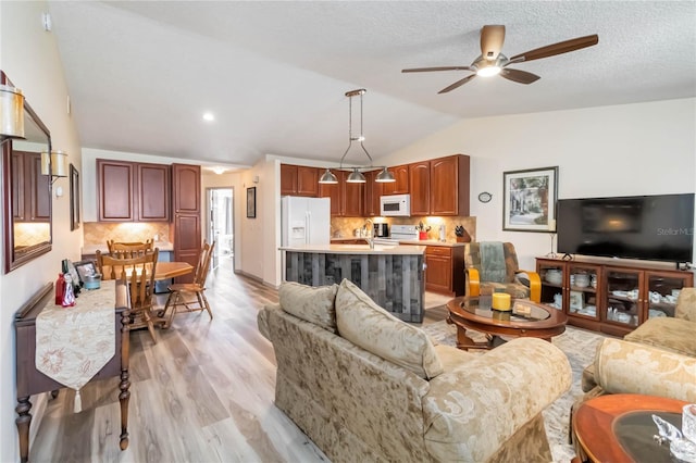 living area featuring lofted ceiling, light wood finished floors, a textured ceiling, and a ceiling fan