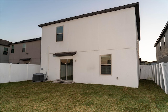 rear view of house featuring central AC, a lawn, fence, and stucco siding