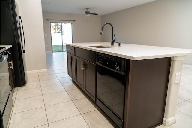 kitchen featuring light tile patterned floors, a sink, light countertops, black appliances, and a center island with sink