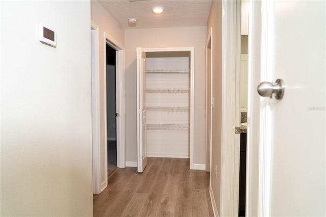 corridor with a textured ceiling, light wood-type flooring, and baseboards