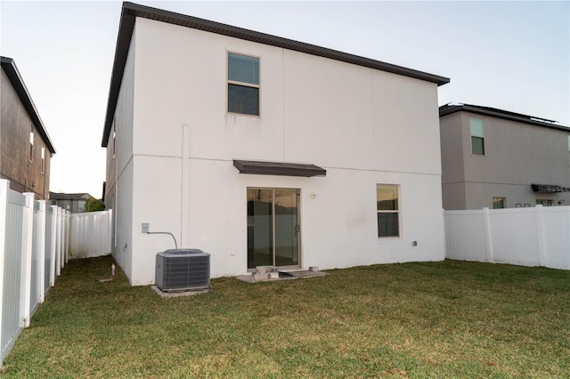 back of house with stucco siding, a fenced backyard, central AC, and a yard