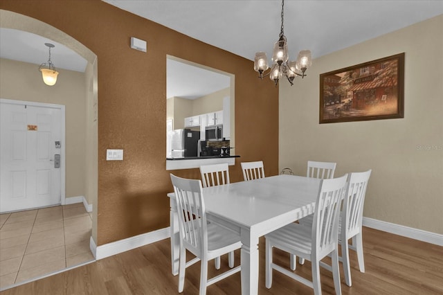 dining room with light wood-type flooring, arched walkways, a chandelier, and baseboards