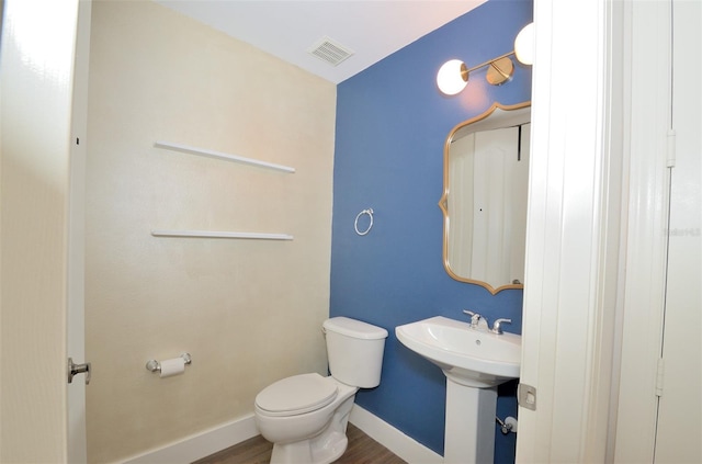 half bath featuring visible vents, toilet, a sink, wood finished floors, and baseboards