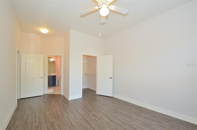 unfurnished bedroom with a walk in closet, baseboards, dark wood finished floors, and a closet