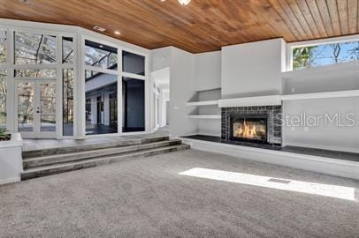 unfurnished living room with wood ceiling, carpet flooring, and a tiled fireplace