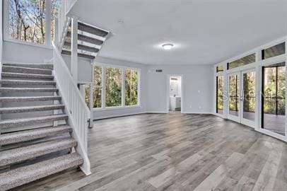 unfurnished living room featuring wood finished floors, french doors, baseboards, and stairs