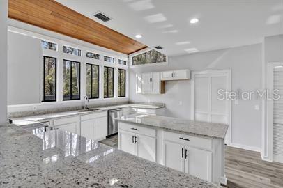 kitchen with a sink, visible vents, white cabinetry, stainless steel dishwasher, and light stone countertops