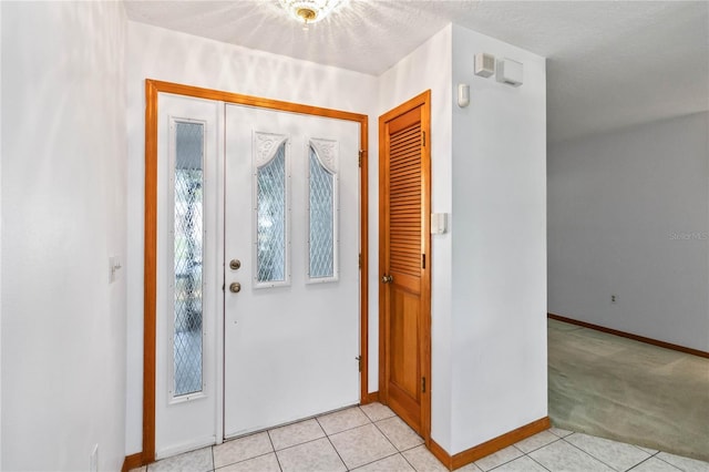 entryway featuring light tile patterned floors, baseboards, and light colored carpet