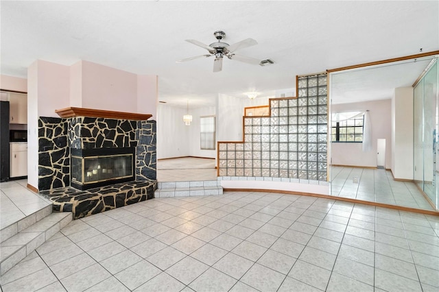 living room featuring light tile patterned floors, visible vents, baseboards, ceiling fan, and a fireplace