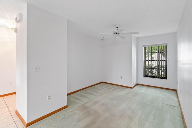 empty room with light tile patterned flooring, ceiling fan, baseboards, and light colored carpet