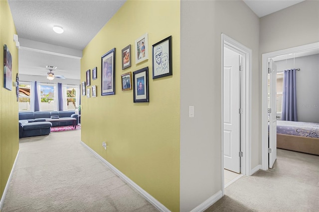 hallway featuring light carpet, a textured ceiling, attic access, and baseboards