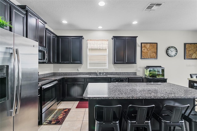 kitchen featuring light tile patterned flooring, a kitchen island, visible vents, appliances with stainless steel finishes, and dark stone counters