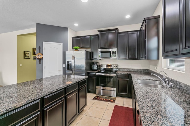 kitchen with light tile patterned floors, stainless steel appliances, dark stone countertops, and a sink