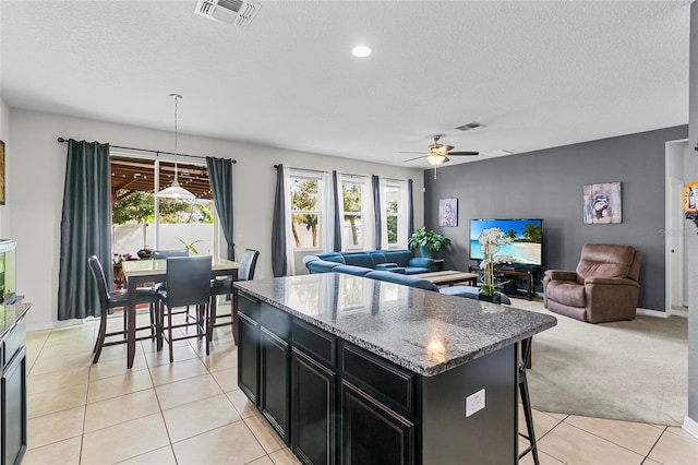 kitchen featuring dark stone counters, a kitchen island, visible vents, and pendant lighting