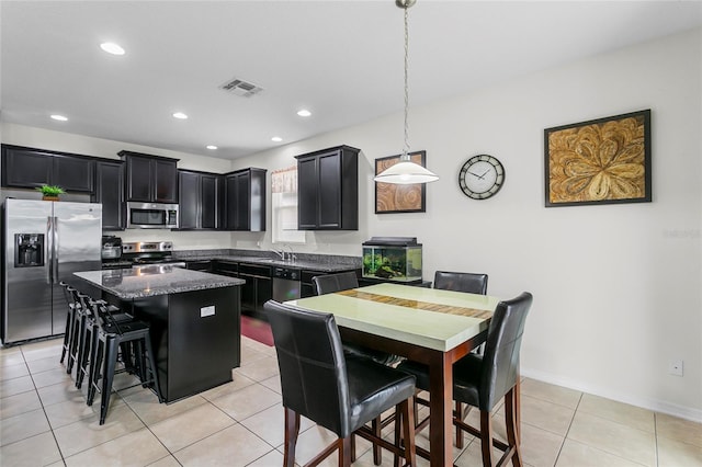 kitchen featuring visible vents, a kitchen island, dark cabinets, stainless steel appliances, and pendant lighting