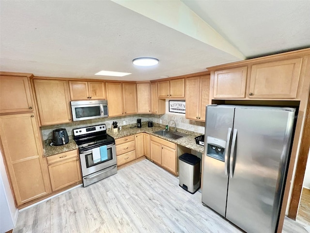 kitchen with appliances with stainless steel finishes, light brown cabinets, a sink, light stone countertops, and light wood-type flooring