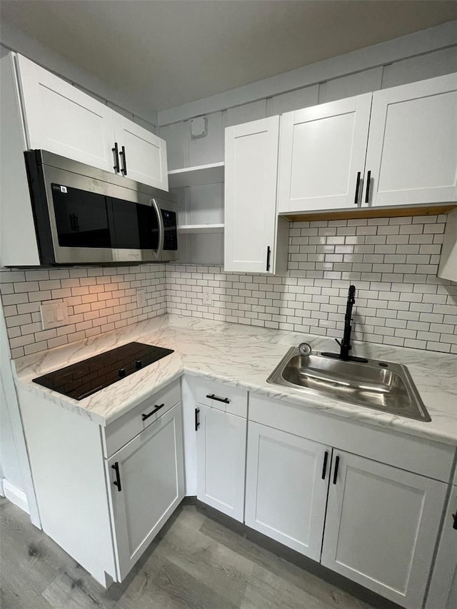 kitchen featuring black electric stovetop, tasteful backsplash, stainless steel microwave, white cabinets, and a sink