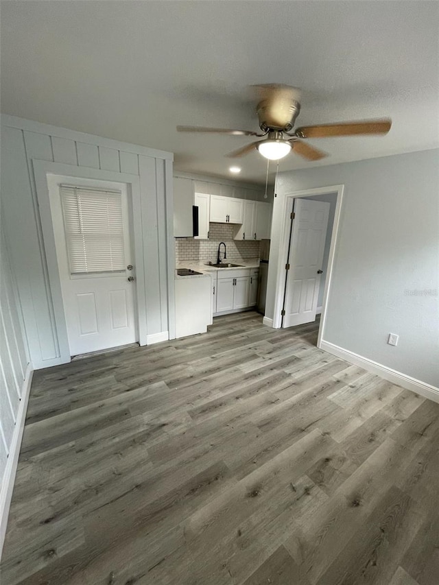 interior space with light wood finished floors, light countertops, decorative backsplash, white cabinetry, and a sink