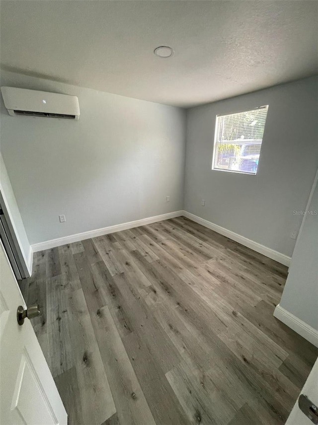 unfurnished room with baseboards, an AC wall unit, and wood finished floors