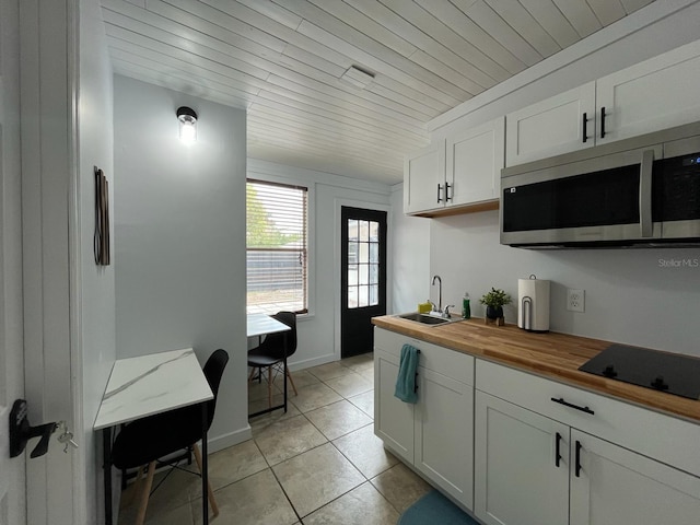 kitchen with stainless steel microwave, white cabinets, a sink, butcher block countertops, and black electric cooktop