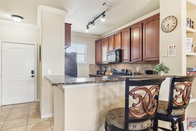 kitchen featuring dark stone counters, black appliances, light tile patterned floors, and a peninsula